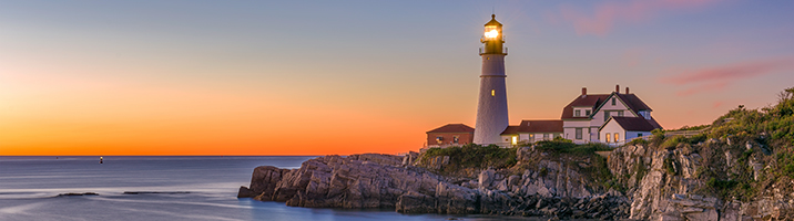 A lighthouse with calm purple waters and an orange sunset