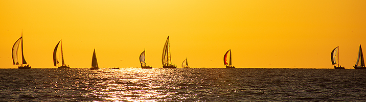 Bright yellow sky with dark water and ships sails in the center
