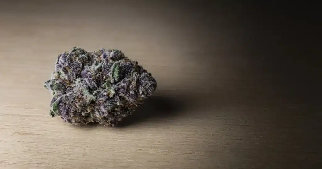 Dense purple cannabis bud with frosty trichomes on a wooden board