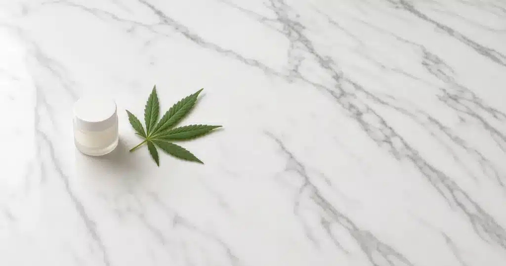 CBD cream jar beside a hemp leaf on a marble counter