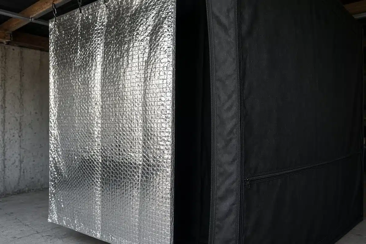 Foil faced bubble insulation hung outside a closed grow tent wall in a basement, with an air gap between them
