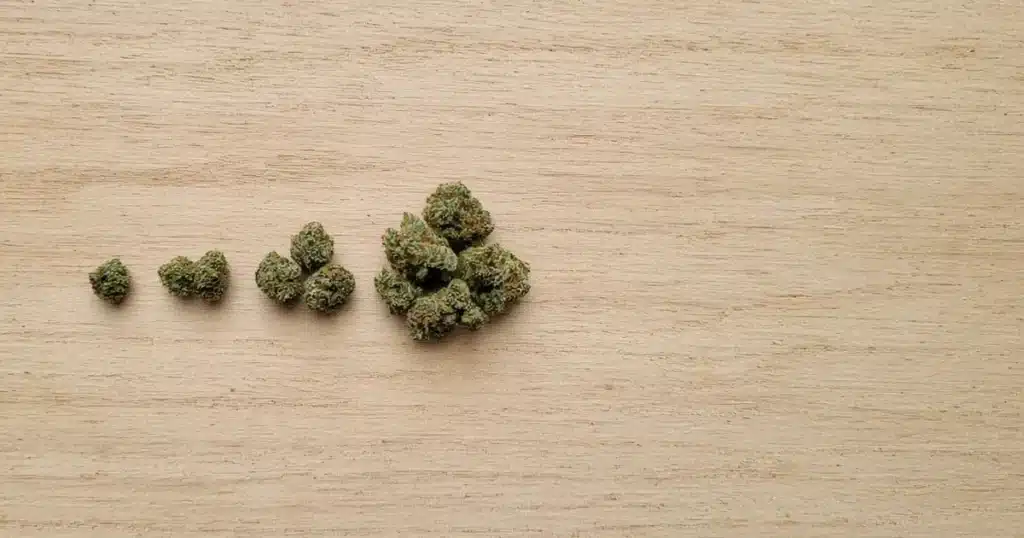 Four piles of cannabis buds from small to large on a wooden board