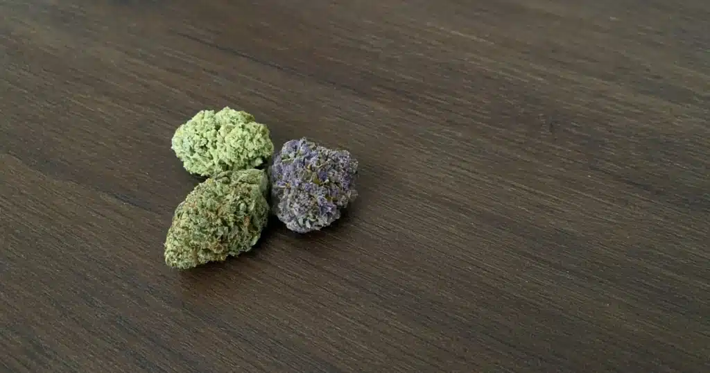 Three different cured cannabis buds on a wooden board