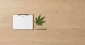 Cannabis leaf beside a blank clipboard on a desk